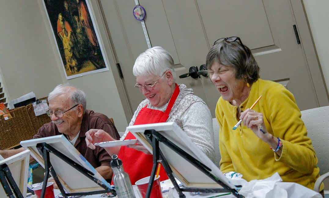 women laughing while painting on canvas during art lass